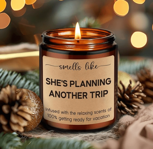 A candle labeled "Smells Like She's Planning Another Trip," surrounded by festive decorations and pinecones.